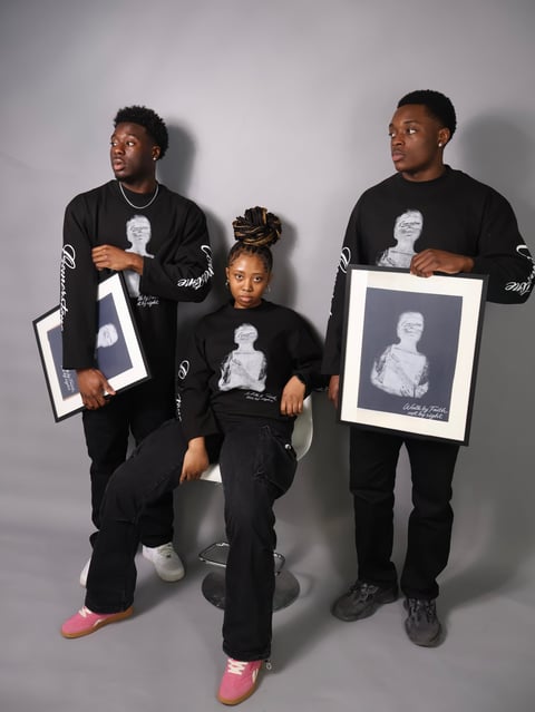 Three people wearing black Cornerstone clothing holding framed portrait artwork against a gray background