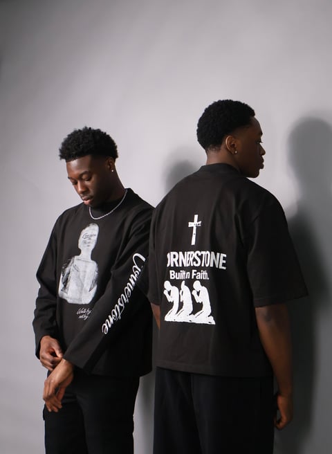 Two young men wearing Cornerstone black graphic t-shirts with religious text and imagery