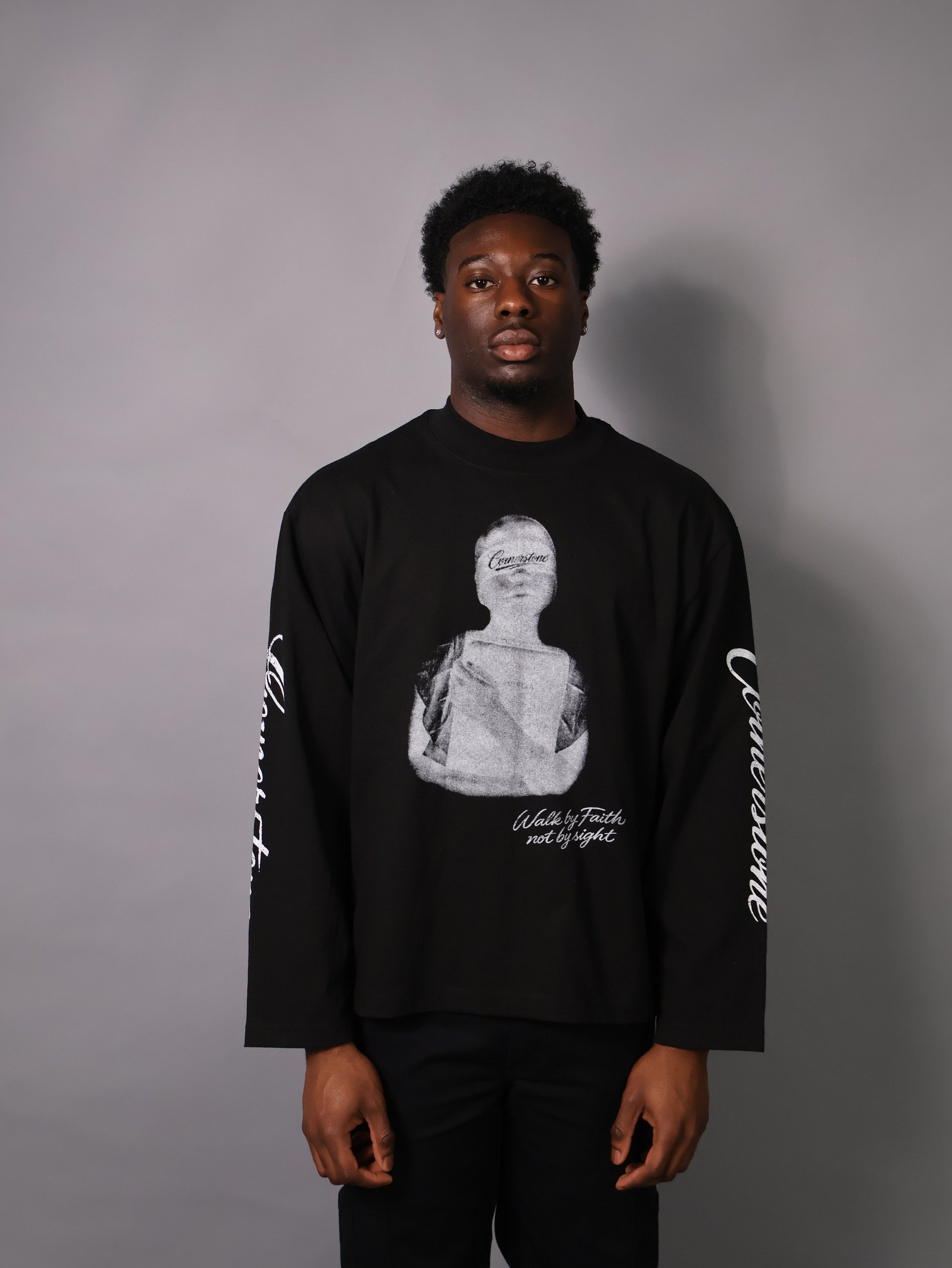 Man wearing black long-sleeve shirt with graphic print and text on sleeves, standing against gray background